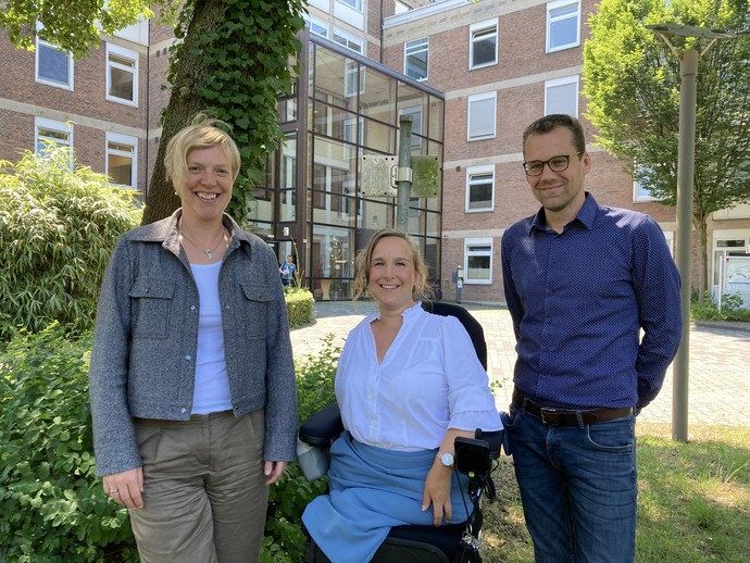 3 Kolleg:innen stehen vor dem Klinikgebäude und lächeln in die Kamera
