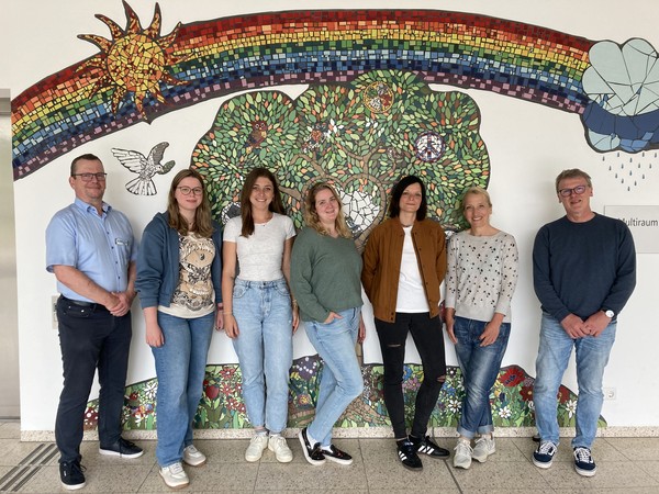 Mitarbeitende der Klinik stehen vor einer Wand mit einem Mosaik.