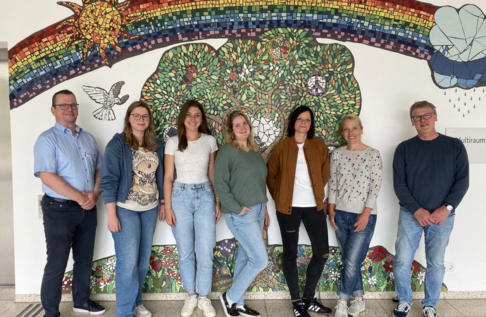 Mitarbeitende stehen vor einer Wand mit einem Mosaik.