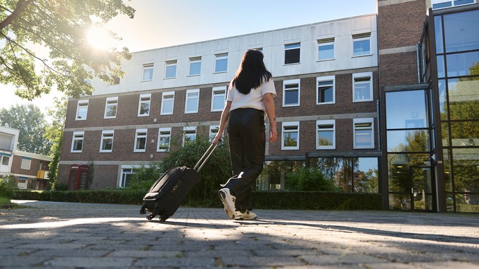 Das Bild zeigt eine Person von hinten, die einen Koffer hinter sich her zieht.