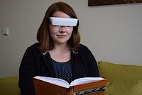 Junge Frau liest ein Buch und trägt dabei eine weiße Lichttherapie-Brille.