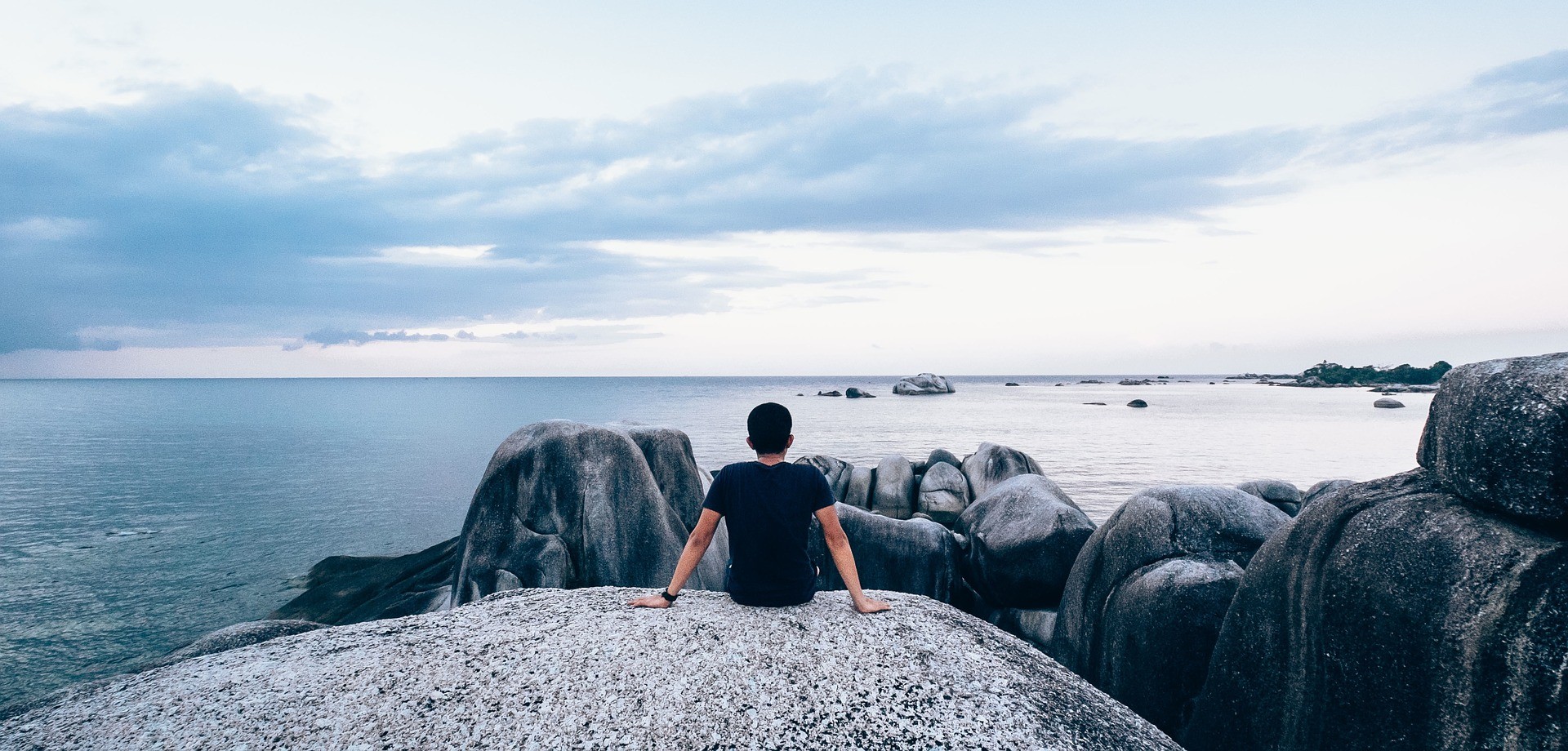 Ein junger Mann sitzt auf einem Felsen und schaut auf das Meer hinaus