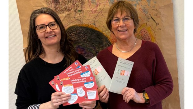 Einladung zur Kunstausstellung, zwei Kolleginnen halten die Einladungen in die Kamera