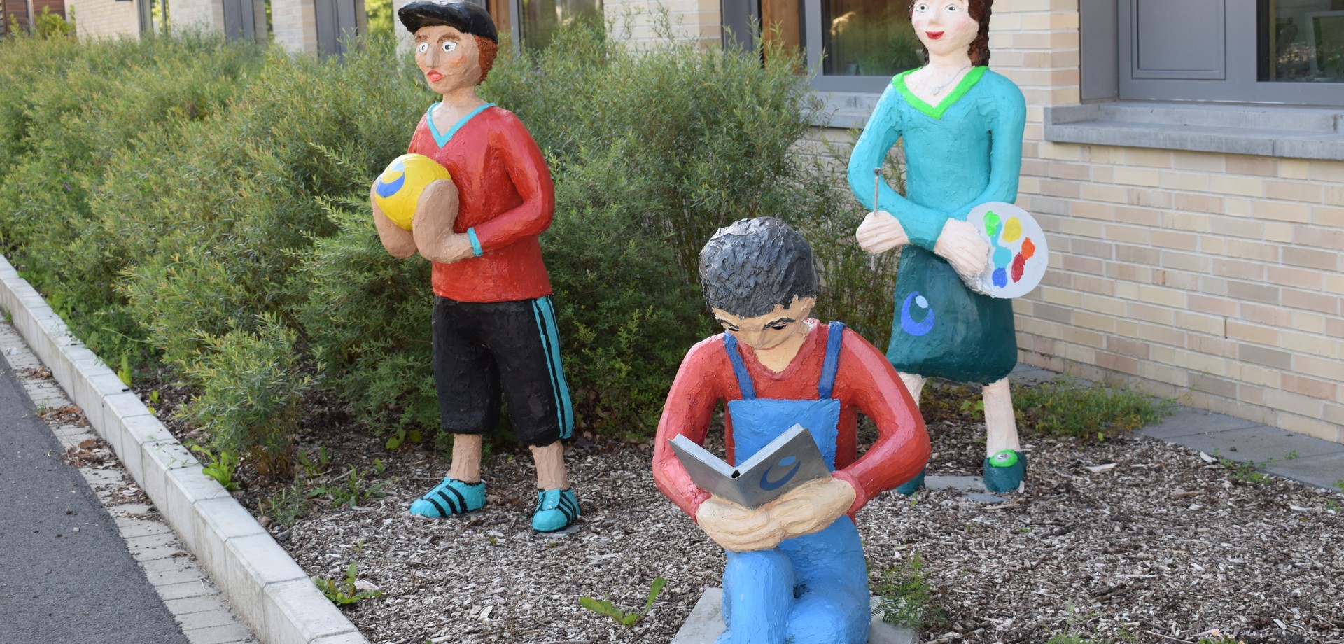 Drei Betonfiguren vor dem Eingang des Schulgebäudes