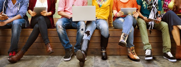 Jugendliche mit Tablets oder Laptops auf den Knien.