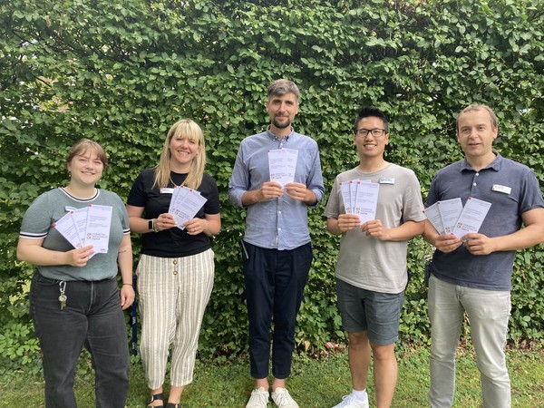 Kolleginnen und Kollegen der WL-Universitätsklinik Hamm halten einen Flyer in der Hand, der zum Fachtag einlädt.