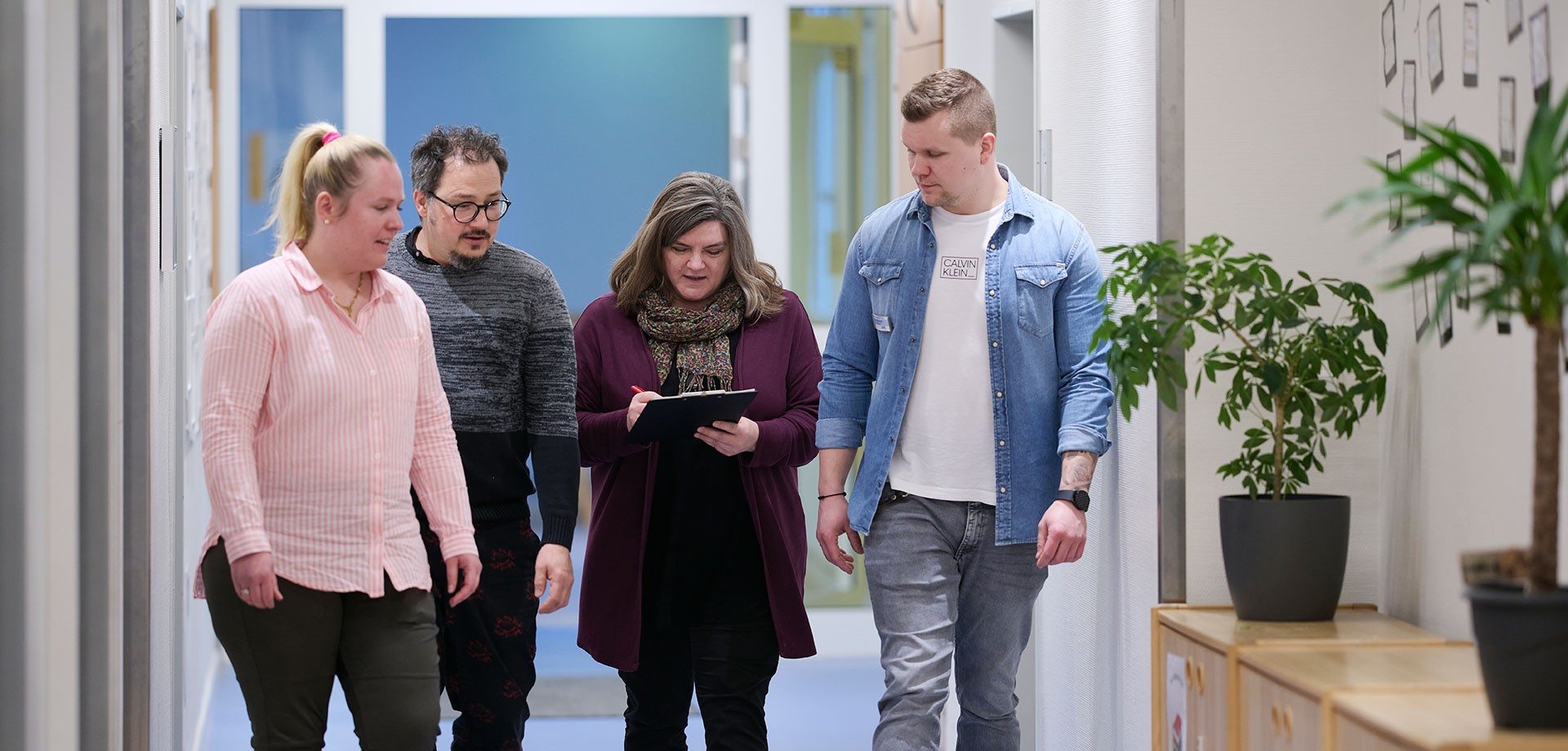Vier Kolleg:innen laufen nebeneinander her und sprechen über ein Dokument.