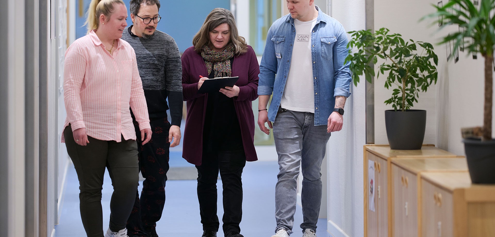 Vier Kolleg:innen laufen nebeneinander her und sprechen über ein Dokument.