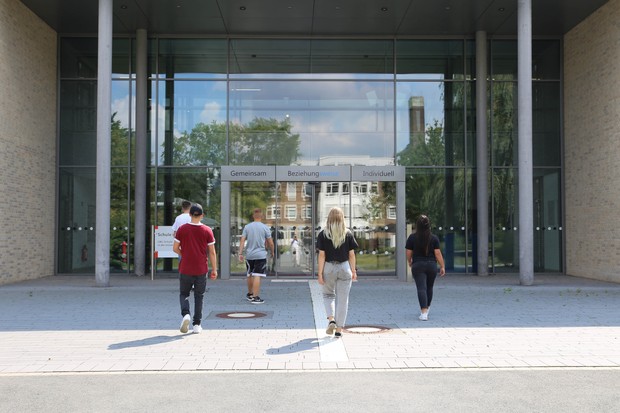 Jugendliche gehen auf ein Eingang der Schule im Heithof zu. Jugendliche gehen auf ein Eingang der Schule im Heithof zu.